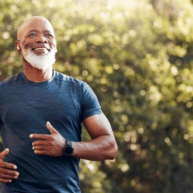 A smiling black man running in the sun in a park.